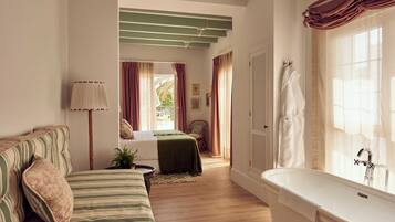 A bedroom with a bed, a nightstand, a lamp, a window with curtains, and a bathroom with a bathtub.