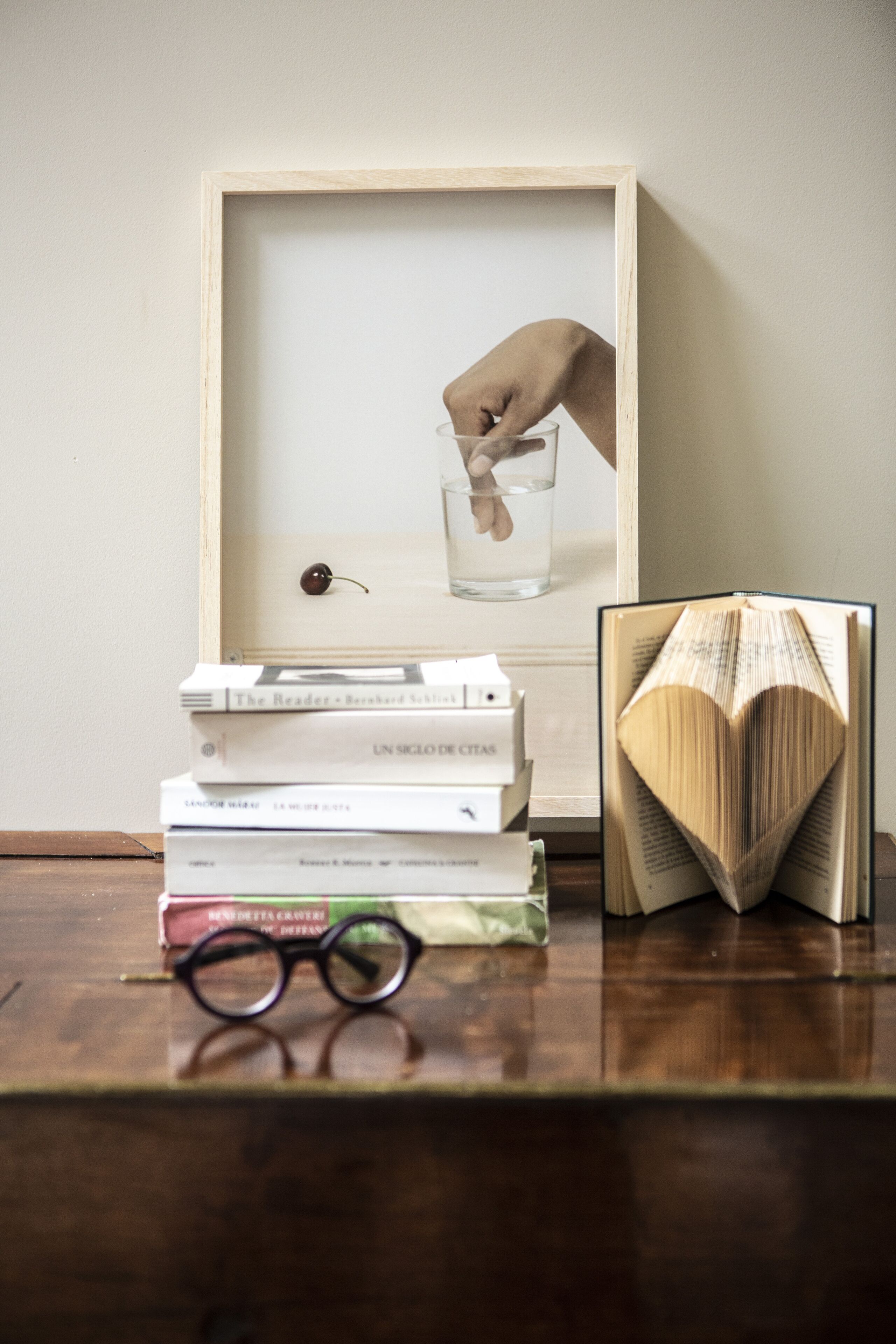 A framed picture of a hand pouring water into a glass, with books and glasses on a wooden surface.