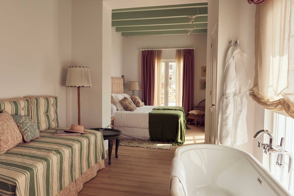A bedroom with a bed, bedside table, lamp, and a view of a balcony.