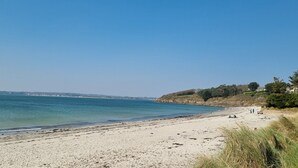 A beach with clear blue water, sandy shore, and some buildings in the background. - Superb Beach Front Apartment in Concarneau (Concarneau)