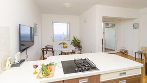 A modern kitchen with a gas stove, a dining table with chairs, a TV mounted on the wall, and a window with a view.