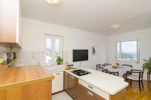 Cozinha moderna com ilha central, área de jantar com mesa e cadeiras, televisão de tela plana na parede e janela com vista para o mar.