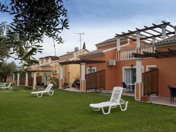 Una zona residencial con un patio techado, sillones blancos y un césped cuidado.