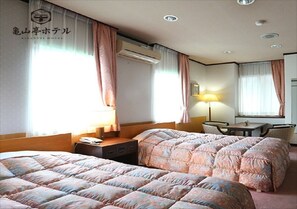 Two beds with matching bedding, a desk, and a window with curtains.
