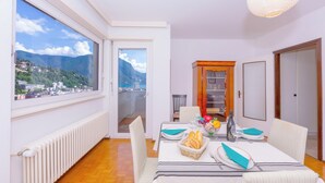 Un coin repas avec une table dressée pour deux personnes, une vue sur les montagnes et une porte donnant sur un balcon.
