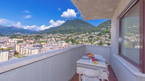 Un balcon avec une table et des chaises, offrant une vue sur un paysage urbain avec des montagnes en arrière-plan.