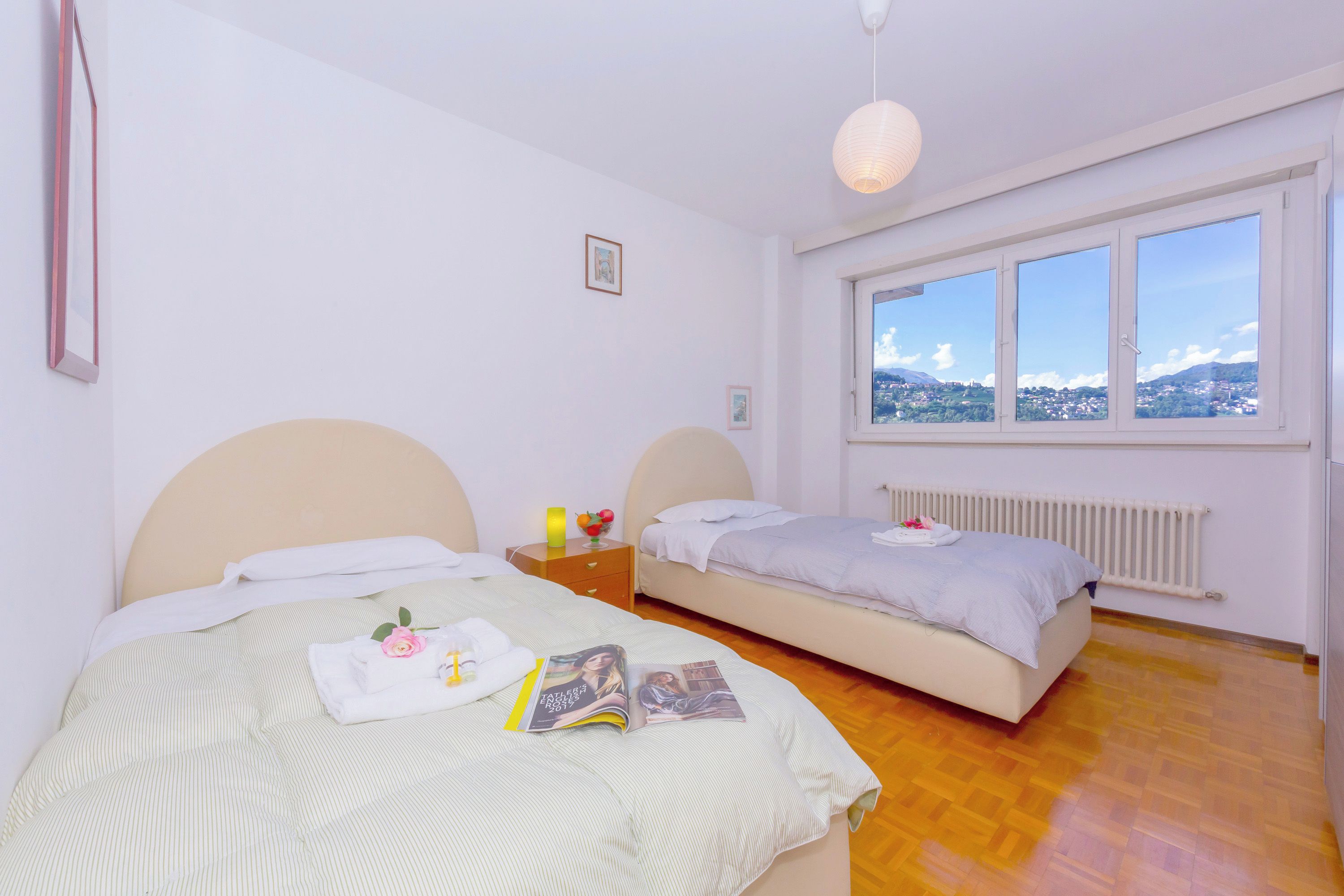 Un dormitorio con dos camas, una ventana con vistas, una mesita de noche y una lámpara colgante.