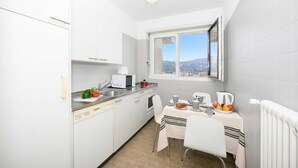 Une cuisine compacte avec des meubles blancs, une table à manger avec des chaises, une fenêtre donnant sur la ville et un radiateur.