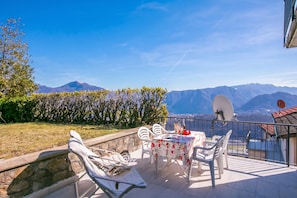 Eine Terrasse mit Tisch und Stühlen, eine Steinmauer und Blick auf Berge.
