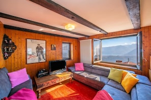 Ein Zimmer mit Holzwänden, einer Couch, einem Fernseher und einem Fenster mit Bergblick.