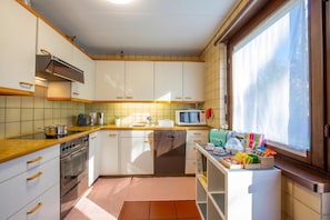 Eine Küche mit weißen Schränken, einem Herd, einem Backofen, einer Mikrowelle und einem Fenster mit Vorhängen.