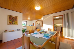 A dining area with a wooden ceiling, a painting on the wall, and a kitchen in the background.