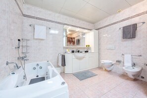 Une salle de bain moderne équipée d’une baignoire, d’un lavabo, de toilettes, d’un bidet et d’un grand miroir.