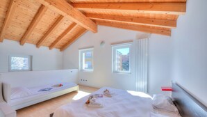Un dormitorio con techo de madera inclinado, dos camas y dos ventanas.