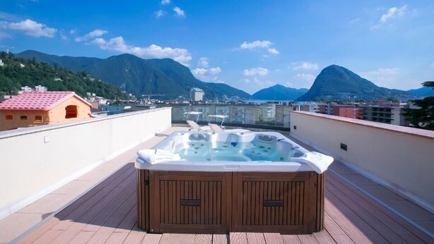 Une terrasse sur le toit avec un jacuzzi, une plateforme en bois et une vue sur les montagnes et les bâtiments.