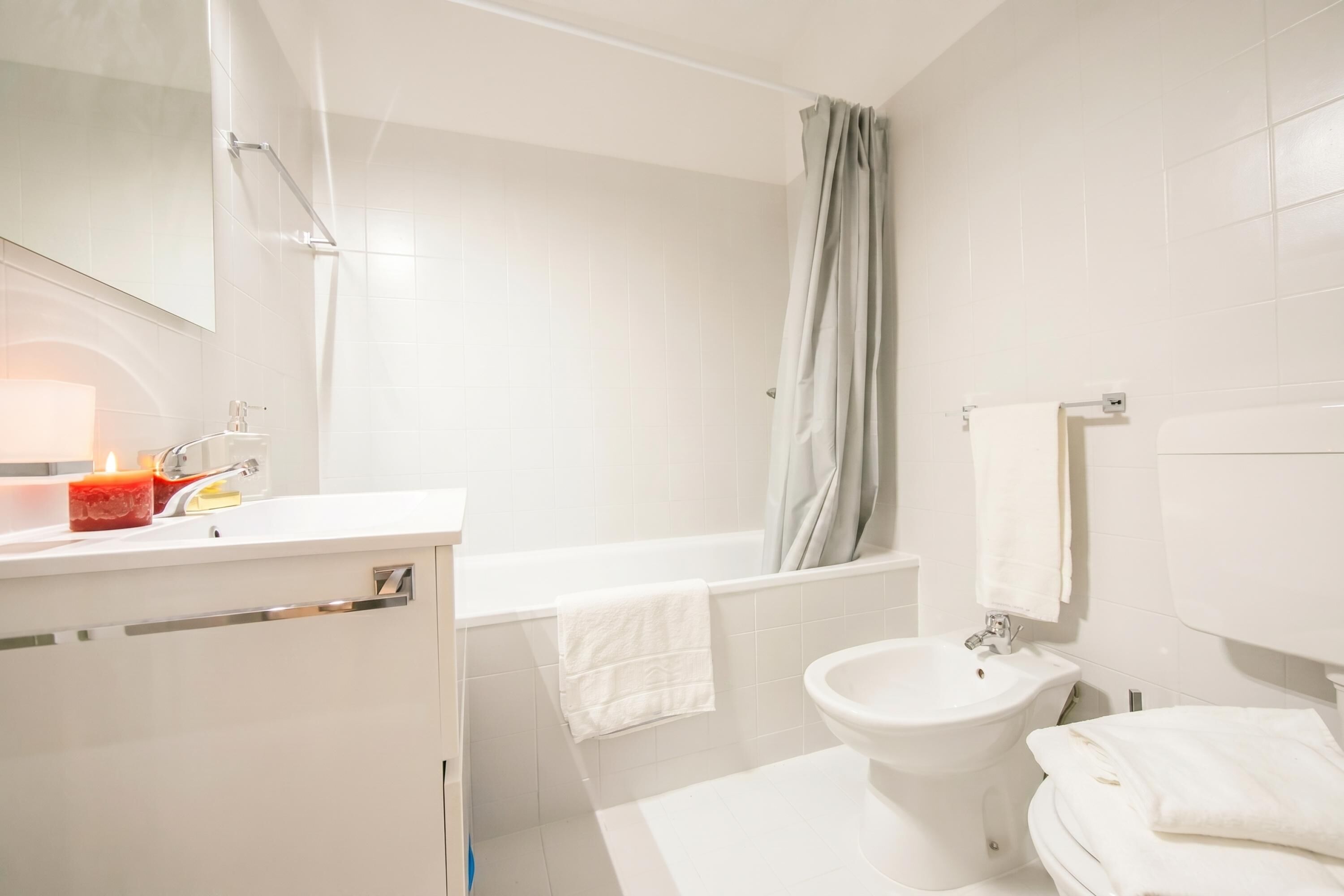 Een moderne badkamer met een wastafel, spiegel, badkamermeubel, badkuip, douchegordijn en een hygiëneslot.