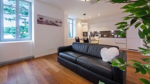 A modern living room with a black leather sofa, a white fluffy pillow, and a large window with a view of trees. - Love of Lugano (Lugano)