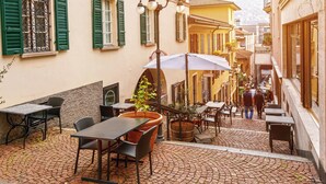 An outdoor café with tables and chairs, a street view, and a mountain in the background. - Love of Lugano (Lugano)
