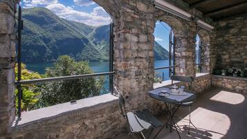 Una habitación con paredes de piedra, una mesa y sillas, con vistas a un lago y montañas.