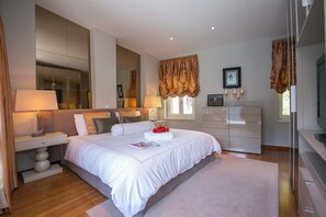 Un dormitorio moderno con una cama grande, lámparas de noche, un aparador, un televisor y un espejo amplio.