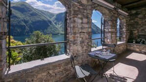 A stone balcony with a table and chairs overlooking a lake and mountains. - Magic Gandria (Lugano)