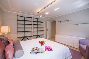Habitación de hotel con cama, mesita de noche, lámpara, una revista y un ramo de flores.