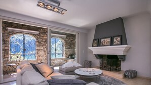 A modern living room with a stone wall, a fireplace, and a large window with decorative ironwork. - Magic Gandria (Lugano)