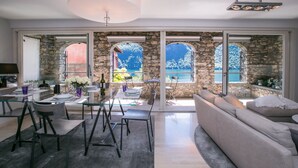 A modern living room with a stone wall, large windows, a sofa, and a dining area with chairs and a table. - Magic Gandria (Lugano)