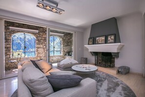 Una sala de estar moderna con pared de piedra, chimenea y un ventanal con vistas.