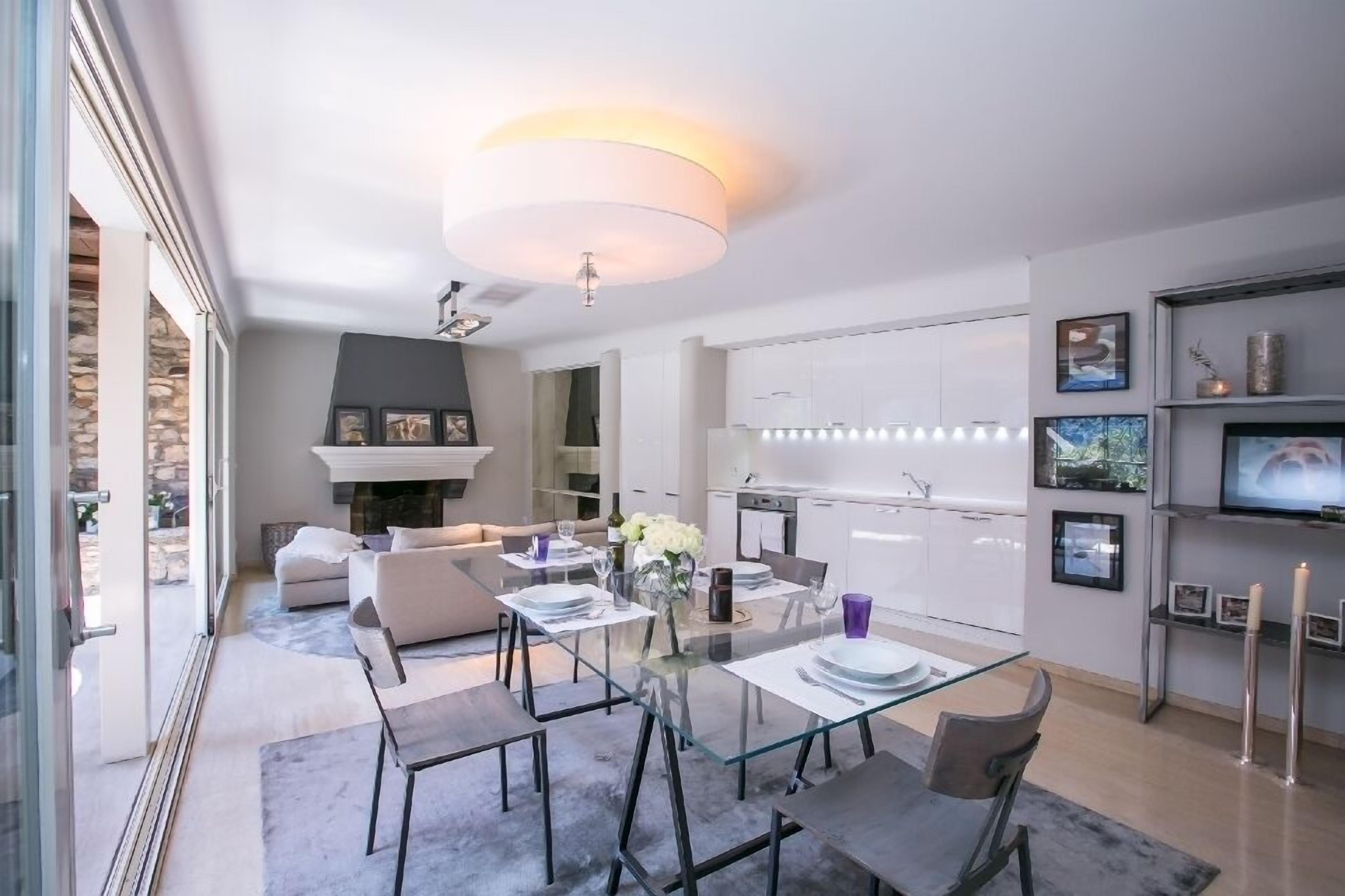 A modern living space with a glass dining table, a fireplace, and a kitchen area.