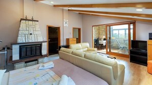 A spacious living area with a stone fireplace, a large beige sofa, and a dining area visible through a glass door. - Apartments Kristina- comfort two bedroom apartment (Rovinj)