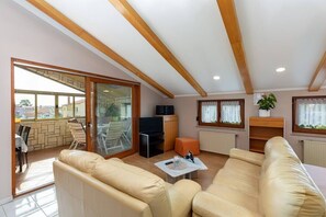 A spacious living room with a large sofa, a television, and a dining area with chairs and a table.