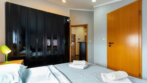A bedroom with a bed, a nightstand with a lamp, a wardrobe, and a wooden door. - Apartments Kristina- comfort two bedroom apartment (Rovinj)
