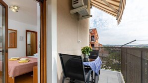 Un balcón con una mesa, una silla y una planta en maceta, con vistas a edificios al fondo.
