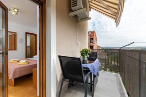 Un balcón con una mesa, una silla y una planta en maceta, con vistas a edificios al fondo.