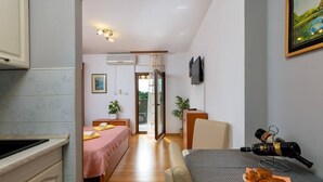Una habitación compacta con kitchenette, una cama, una mesa de comedor y una botella de vino, y un televisor montado en la pared.