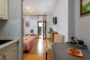 Une pièce compacte comprenant un coin cuisine, un lit, une table à manger avec une bouteille de vin, et un téléviseur fixé au mur.