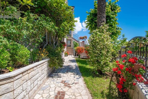 Un sendero de piedra conduce a un edificio con escaleras, rodeado de exuberante vegetación y plantas en flor.