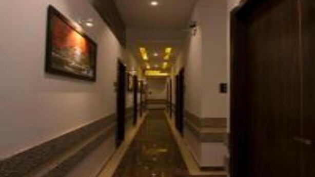 A hallway with a marble floor, a framed picture on the wall, and a wooden door at the end. - Hotel Meriton (Mumbai)