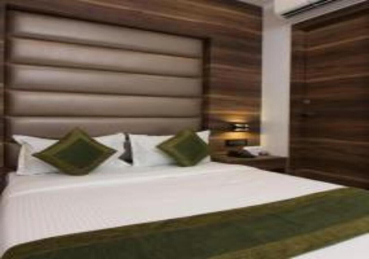 A hotel room with a large bed, a wooden headboard, and a green throw blanket.