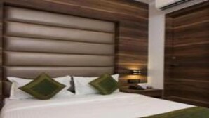 A hotel room with a large bed, a wooden headboard, and a green throw blanket. - Hotel Meriton (Mumbai)