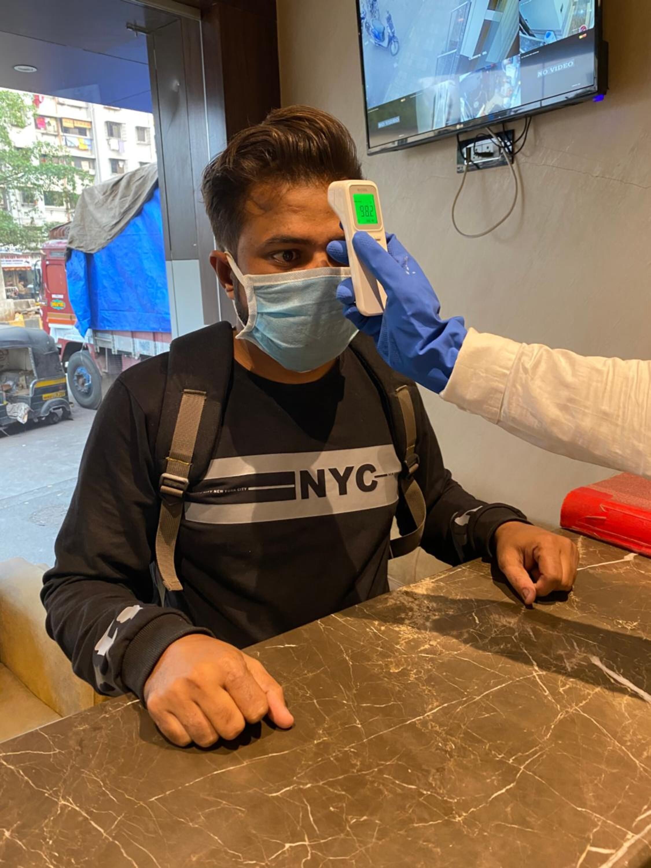 A person wearing a mask and a black shirt with "NYC" on it, being scanned by a device.