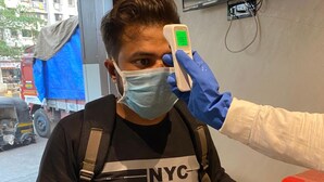 A person wearing a mask and a black shirt with "NYC" on it, being scanned by a device. - Hotel Meriton (Mumbai)