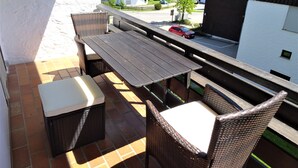 A balcony with wicker furniture, a view of a street, and houses in the background. - Apartment foresight (Steibis)