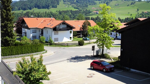 A residential area with modern houses, a parking lot, and a road leading to a hilly landscape. - Apartment foresight (Steibis)