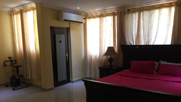 Une chambre à coucher comprenant un lit, une table de chevet, un appareil de climatisation, une porte et un vélo d’exercice.
