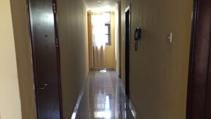 Un long couloir étroit, avec un sol carrelé, une porte sur la gauche et un téléphone sur la droite.