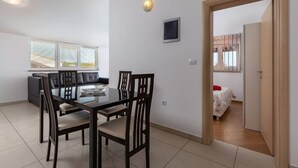 A dining area with a glass table and wooden chairs, a sofa, and a window with blinds. - Apartment with pool in Medulin A2 (Medulin)