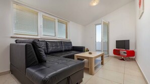 A modern living room with a sectional sofa, a small wooden table, a red entertainment unit, and large windows with blinds. - Apartment with pool in Medulin A2 (Medulin)
