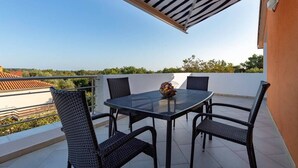 A balcony with a glass table and four wicker chairs, a striped awning, and a clear view of the surrounding landscape. - Apartment with pool in Medulin A2 (Medulin)